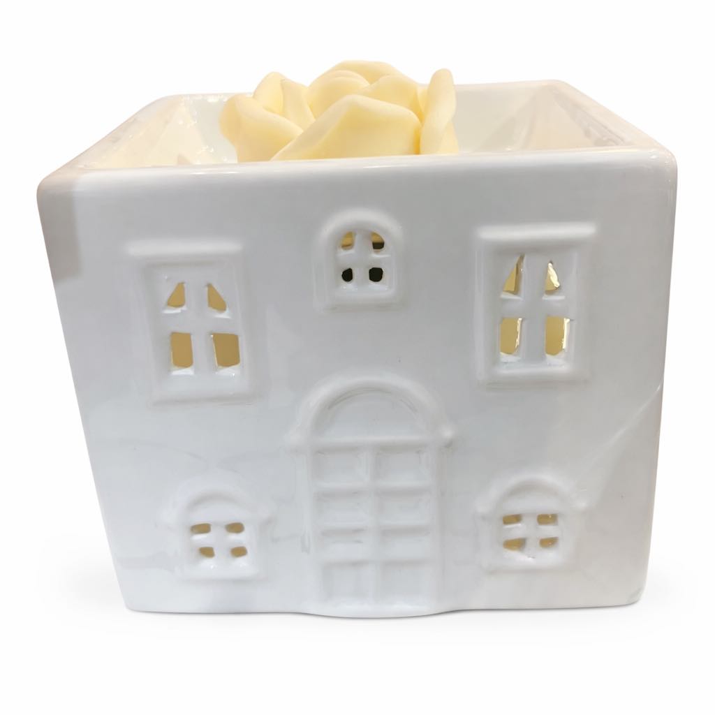 White ceramic house-shaped candle holder with a small candle inside on a white background