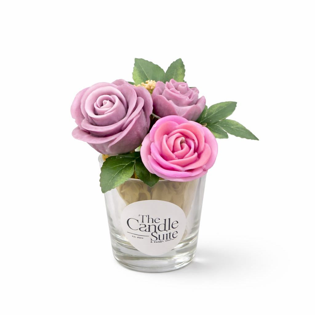 Decorative candle with pink and purple flowers and green leaves on a white background, branded 'The Candle Suite'.