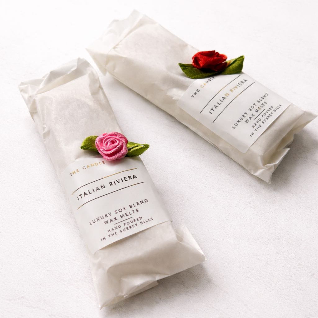 Two wrapped wax melt squares with floral decorations on a white background