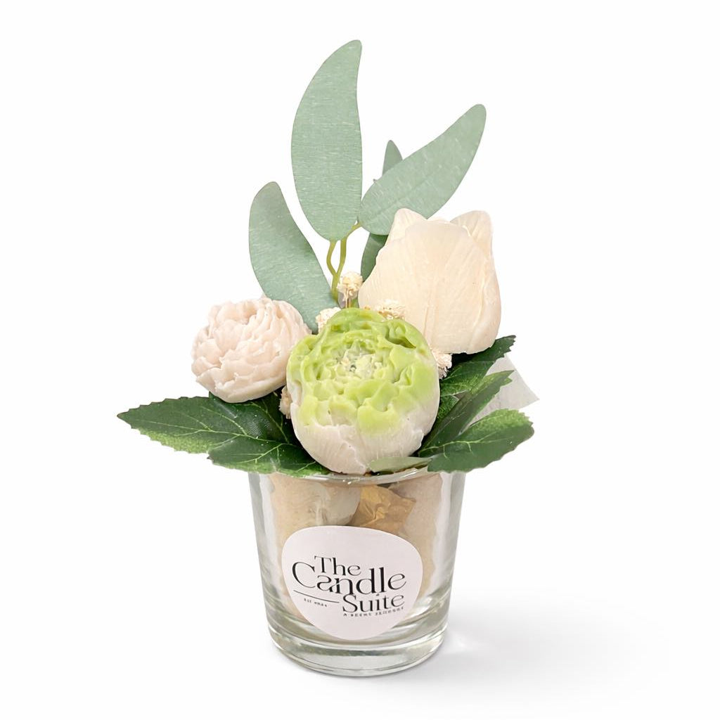 Decorative candle with flowers and leaves in a glass container on a white background