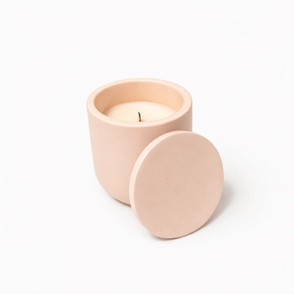 Pink candle in a matching container with lid on a white background