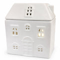 White ceramic house-shaped wax burner with small lights inside on a white background