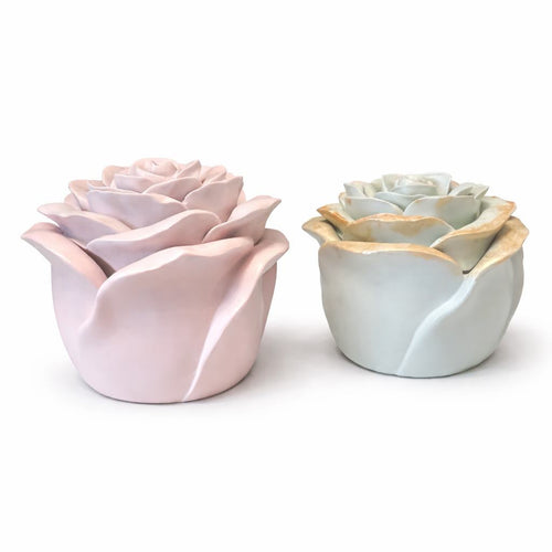 Two ceramic rose-shaped candle jars, one pink and one light blue, on a white background.
