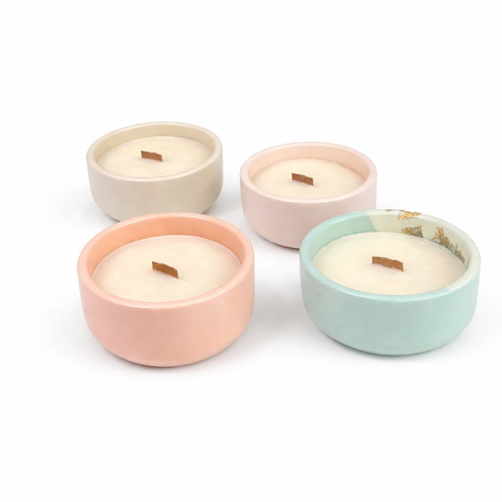 Four small candles in pastel ceramic holders on a white background