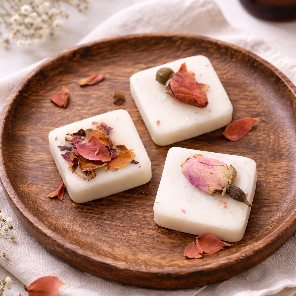 Three wax melt square with dried flowers on a wooden plate, surrounded by small flowers and a candle.