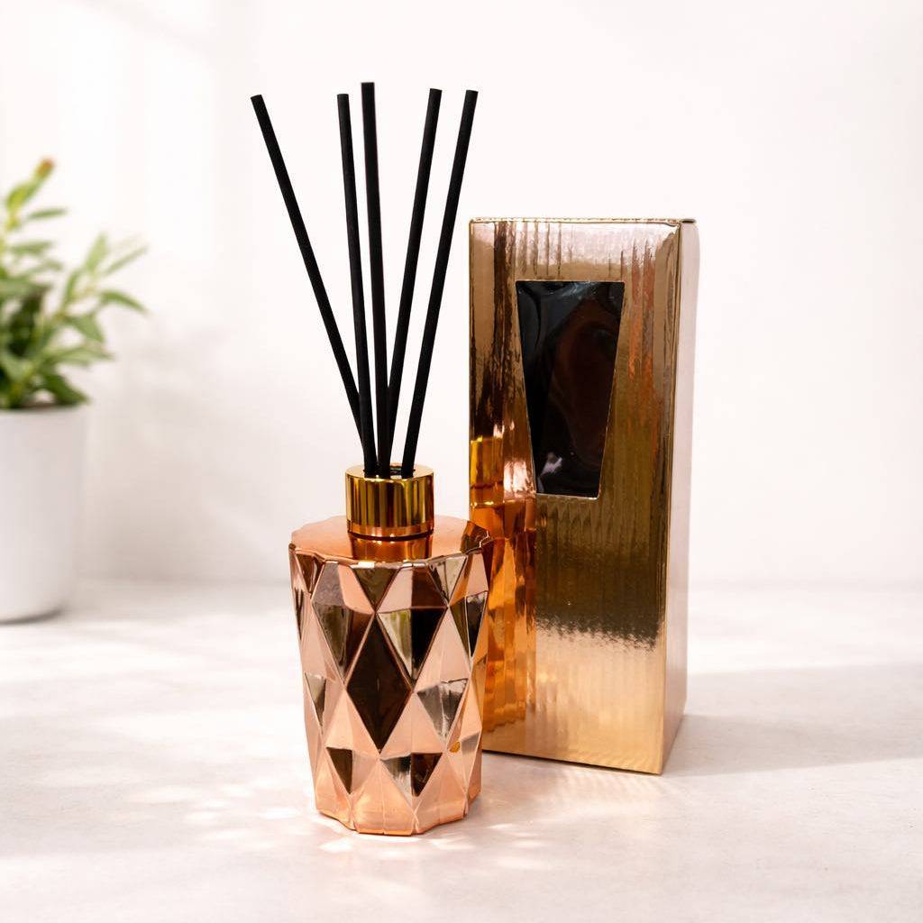 Rose gold glass  diffuser with black reeds on a white surface
