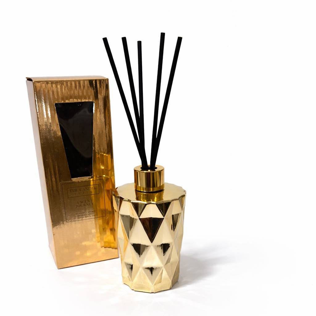 Gold geometric diffuser with black reeds on a white background