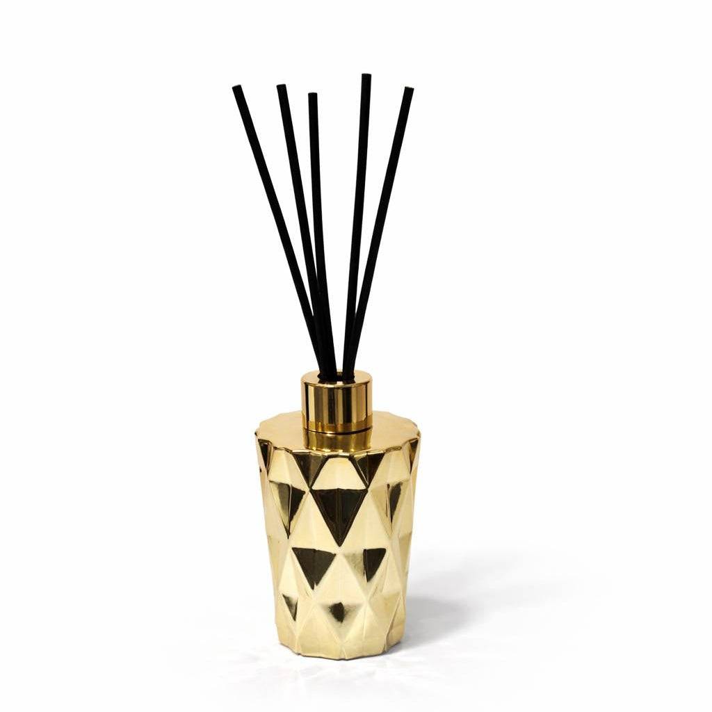 Gold geometric diffuser with black reeds on a white background