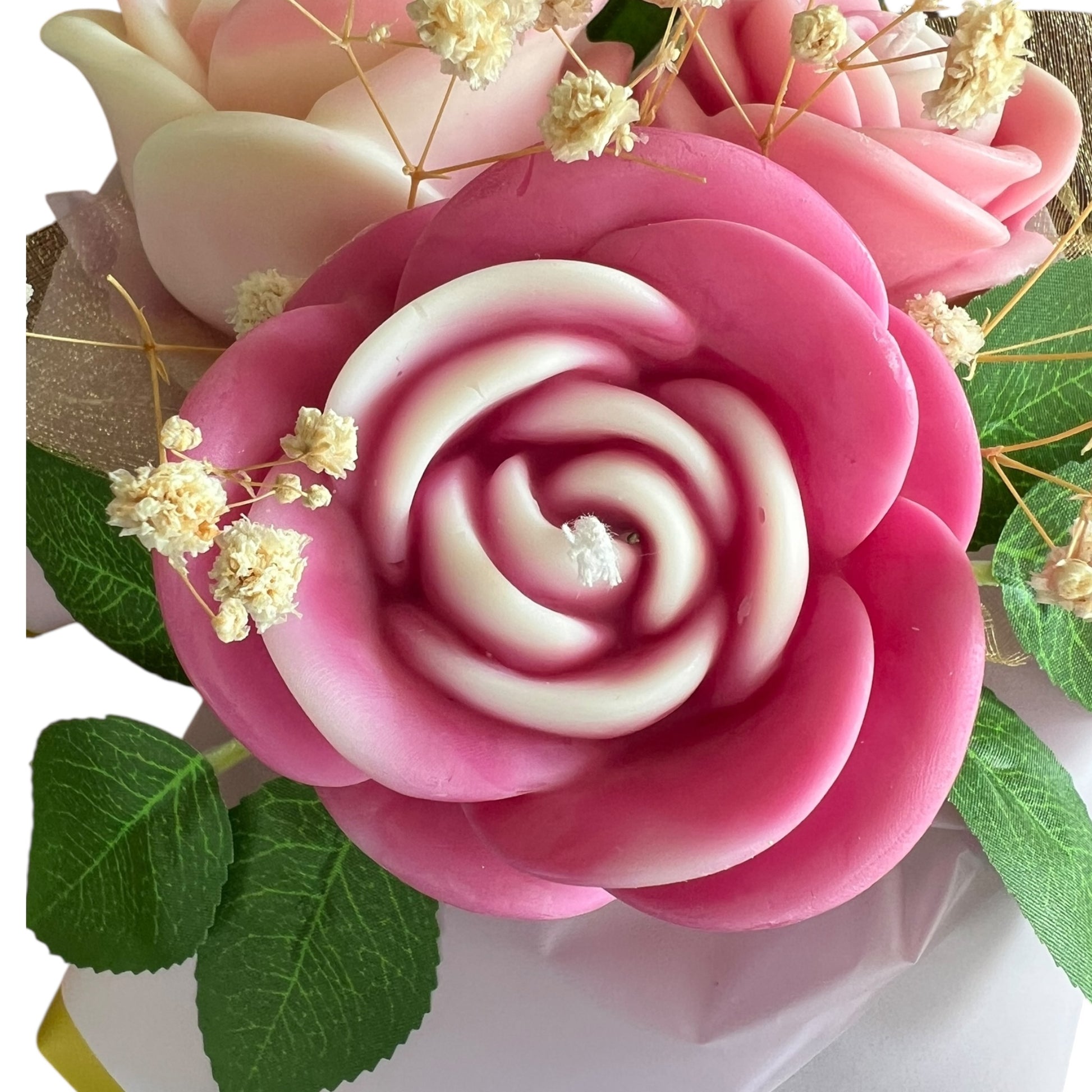 Close-up of a pink and white rose-shaped candy with green leaves and small flowers in the background.