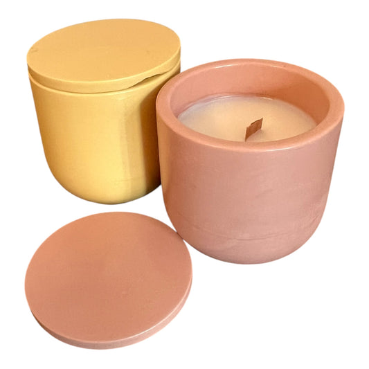 Two handmade containers, one yellow and one pink, with a candle inside the pink container on a white background.