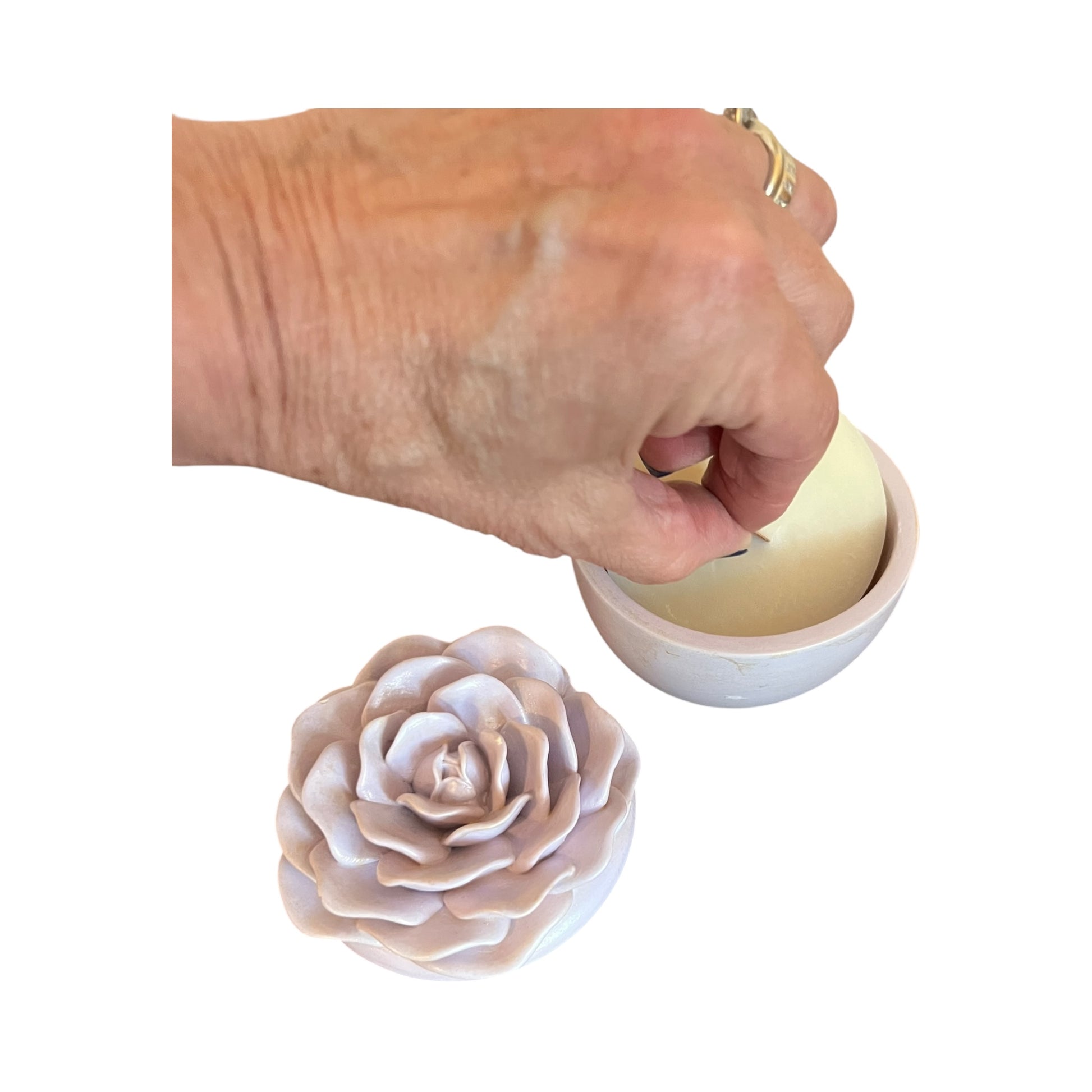 Hand holding a small white candle next to a flower-shaped candle mold on a white background